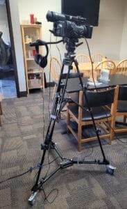 Tripod on wheels with camera mounted, headphones and mic plugged in